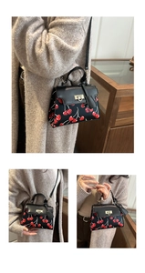 Detail showing red cherry print on black leather bag with metal buckle and shoulder strap