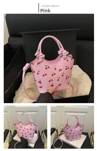 Detail of pink shoulder bag with cherry print, featuring knotted handle and strap