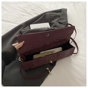 Detailansicht der weinroten Handtasche mit Schlangenmuster auf grauem Anzug