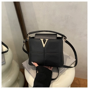 Detail of black lychee grain leather tote bag with iconic gold V metal buckle and strap