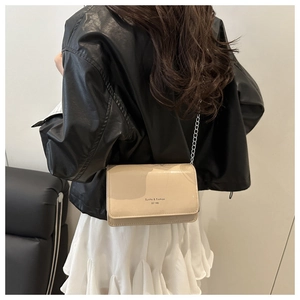 Détail d'un sac bandoulière en cuir verni beige avec chaîne argentée sur un modèle