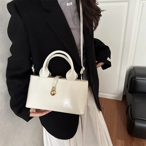 Detail of a creamy beige tote bag with a gold gourd pendant shown on a model