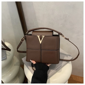Detailed shot of brown litchi leather bucket bag with gold V logo on white pillar
