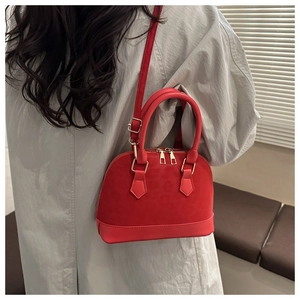 Side view of a red shell bag worn with a gray coat, showing textured panel and gold hardware