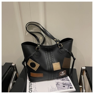 Detail of black leather tote bag with vintage patches and long straps on a chair