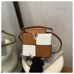 Close-up of brown and white leather handbag with golden V buckle on a stone pedestal