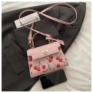 Pink shoulder bag with cherry pattern and gold clasp next to a phone for size reference