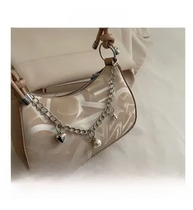 Detail of beige monogram baguette bag with gold heart chain and pearl charms on a blazer