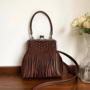 Vintage brown leather crossbody bag with tassel fringe and metal rivets on wooden desk