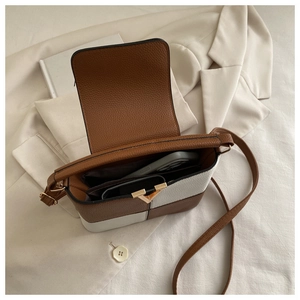 Detail of color-block crossbody bag showing golden V-clasp and interior storage capacity