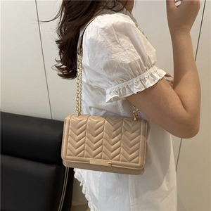Sac à bandoulière matelassé beige élégant avec chaîne dorée porté par un mannequin