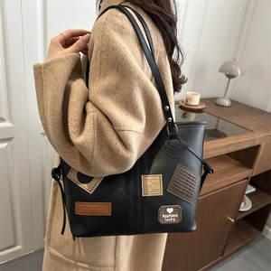 Close-up of black leather tote bag featuring retro patches and heart lucky charms