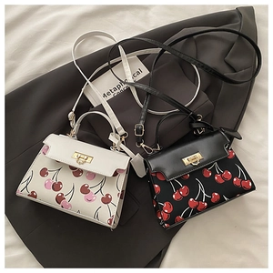 Detailed view of cherry print shoulder bags in black and white on a gray suit jacket