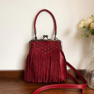 Vintage burgundy crossbody bag with fringe tassels and rivet details on dark wood table