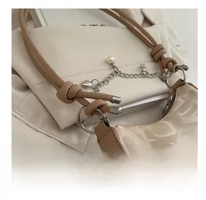 Close-up of beige shoulder bag with silver hardware, pearl charms, and knot strap detail