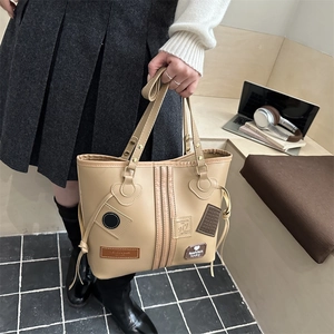 Close-up of a beige faux leather tote bag with patchwork text and side drawstring detail