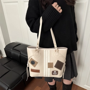 Detail of off-white tote bag with fashion patches and double handles on a leather sofa