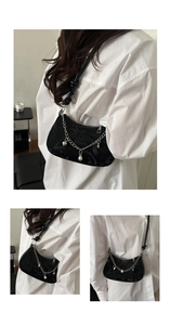 Detail of black underarm bag featuring patterned fabric and silver chain with charms