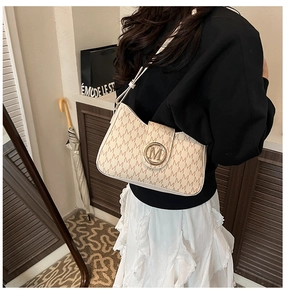 Dettaglio della fibbia in metallo dorato su borsa a tracolla beige con motivo monogramma