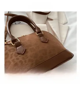 Detail of dark brown patchwork shell bag with golden hardware and suede texture