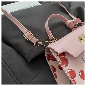 Detail of pink cherry print bag showing golden metal lock and adjustable shoulder strap
