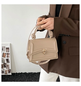 Detail of beige trapezoid handbag featuring knotted handle and gold twist lock closure