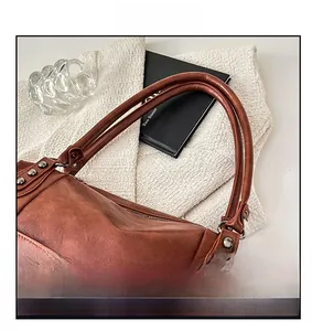 Close-up of brown leather handbag featuring vintage rivets and reinforced handle detail