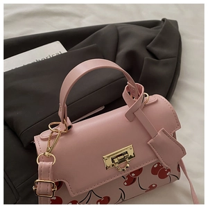 Close-up of pink shoulder bag with cherry print, golden metal lock and PU leather strap