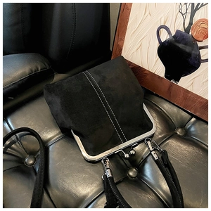 Detail of a black suede bag featuring silver metal clasp and white double stitching