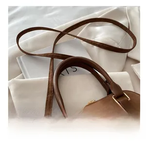 Detail of adjustable strap and golden metal buckle on brown faux suede handbag