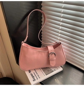 Detail of pale pink underarm bag with silver buckle strap resting on a book
