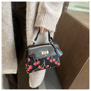 Close-up of black leather lock bag with red cherry print and gold metal clasp
