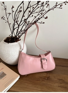 Detailed view of pink French baguette bag with silver metal buckle on a wooden desk