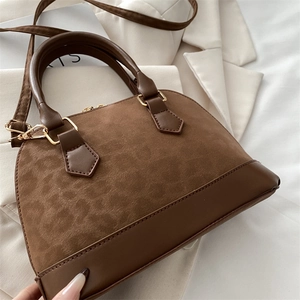 Detail of shell-shaped handbag showing brown suede and smooth leather splicing with gold hardware