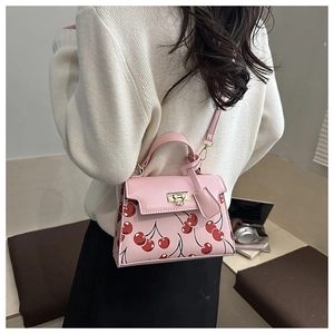 Detail view of pink shoulder bag with cherry print and golden hardware on a model