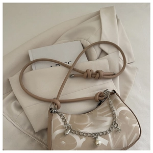 Close-up of beige half-moon bag with elegant knot strap and silver charm chain