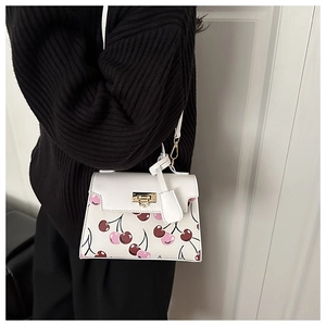Detail of white crossbody bag with pink cherry print and gold lock worn by a model