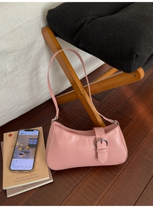 Pink baguette underarm bag with large silver metal buckle on a minimalist wooden stand