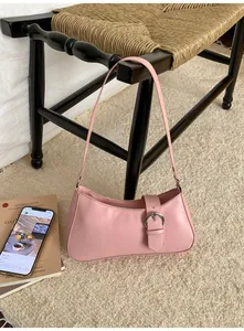 Pink baguette bag with silver buckle strap hanging on a black woven chair in a cozy room