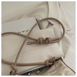 Detail of beige shoulder bag strap with knots, metal buckle and decorative pearl chain