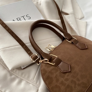 Detail of brown suede shell bag featuring dual gold zippers and sleek leather handle