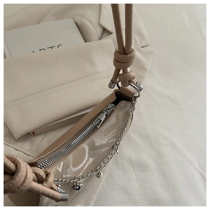 Close-up of beige underarm bag featuring knotted handle and silver heart pendant chain