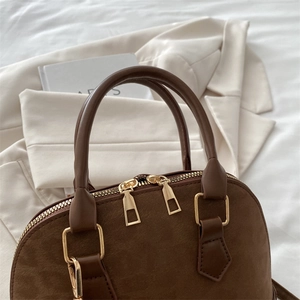Detailed view of brown suede and leather handbag with gold zippers and metal hardware