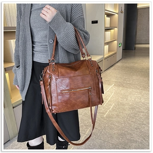 Brown soft leather tote bag with zip detail and tassel shown on model in a warm room