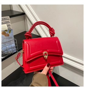 Detail of red leather handbag showing twisted handle and gold oval twist-lock closure