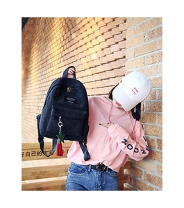 Close-up of black corduroy backpack with star pendant and red tassel on front zipper pocket