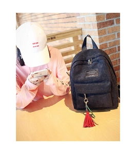 Detail of black corduroy backpack with letter patch and vibrant red tassel accessory