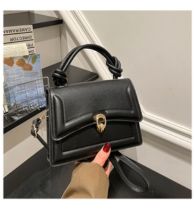 Detail of a black structured handbag with an artistic knot handle and gold buckle closure