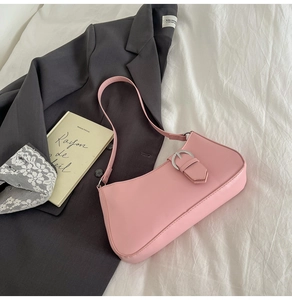 Detail of pink French baguette bag with silver buckle on grey blazer and book