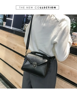 Borsa a tracolla nera con chiusura girevole mostrata su un bancone da caffè moderno